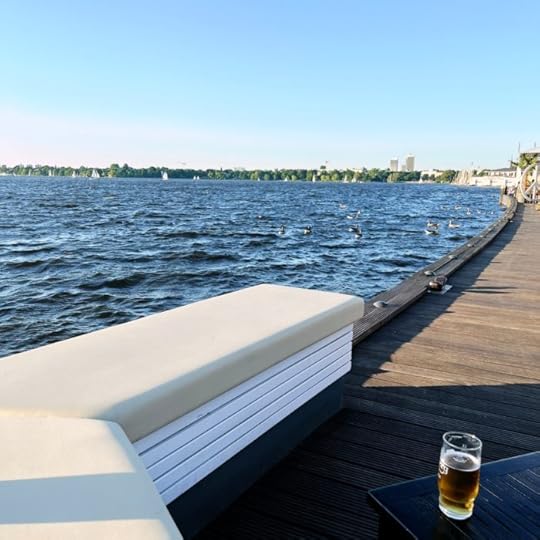 Ein Steg an der Alster, eine Bank mit Sitzpolster darauf, daneben ein Glas Bier