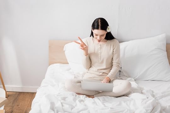 young woman on bed, with laptop, displaying peace or victory gesture