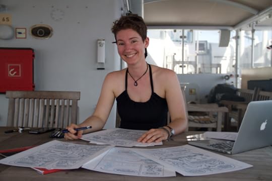 Lucy smiling with a spread of her comics pages on the table in front of her.