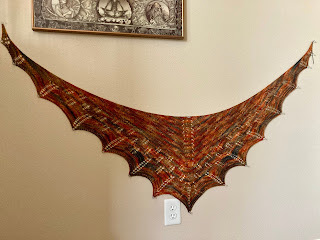 a shawl shaped like the outstretched wings of a dragon in orange/yellow/black dyed yarn, pinned to a wall