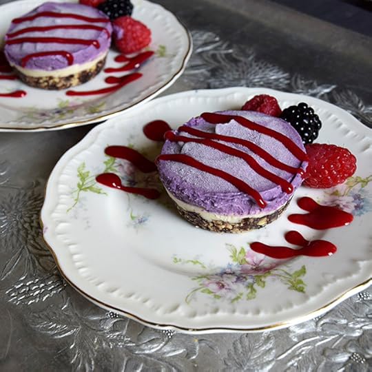 Vegan lemon-blueberry cashew cheesecake drizzled with raspberry coulis and with fresh raspberries and a blackberry
