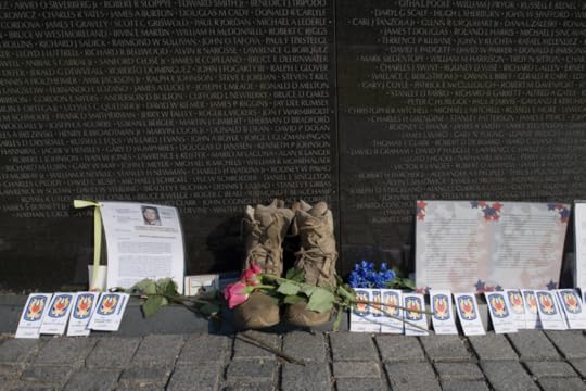Color photo of cards, letter and other items left in front of names of the the Vietnam Memorial. In center of photo is a pair of military boots with a rose laid across them.