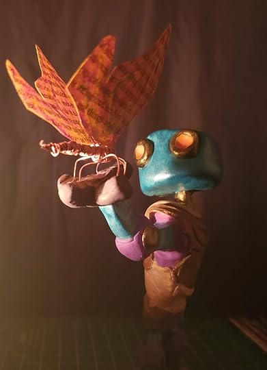 A mixed media sculpture of a robot holding a colorful butterfly. The robot is made of polymer clay and the butterfly is made of wrapped wire with paper wings.
