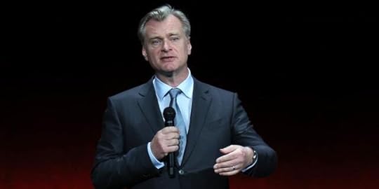 Christopher Nolan speaks on stage and holds a microphone while promoting his film