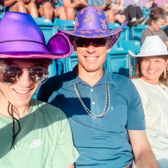 William, Peter, and Amy Julia wear cowboy hats and smile for a selfie as they sit in stadium seating