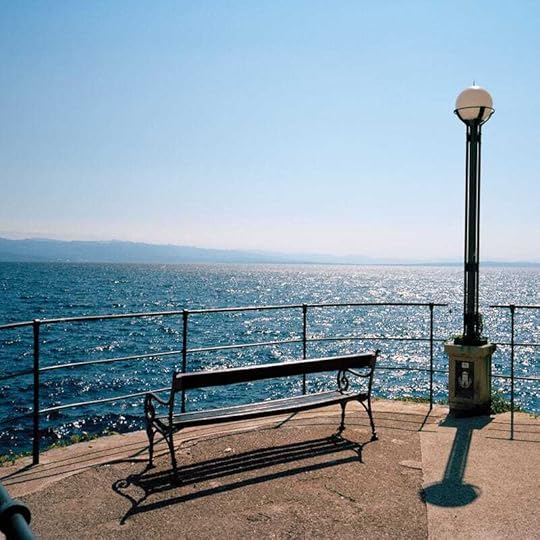 An empty bench beside a street light at the end of a peer overlooking a body of water with moutains in the distance.
