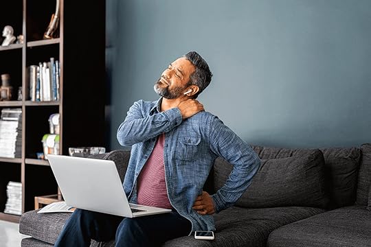 Man sitting on couch with laptop on lap, uncomfortable due to back pain with hands on shoulder and back.