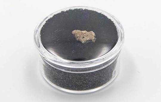 A small chunk of Trinitite in a clear round container.