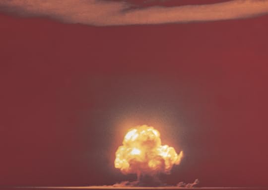 Color photo of the world's first atomic explosion, take from a great distance. The fireball, just starting to mushroom, is at the very bottom of the frame. The rest of the sky is a dark red color, likely from exposure adjustments to account for the pre-dawn sky.