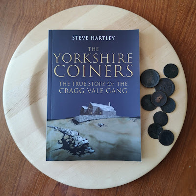Front cover of The Yorkshire Coiners by Steve Hartley on wooden plate with collection of Georgian coins