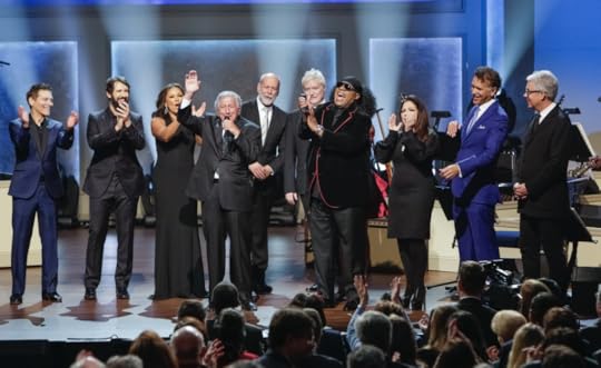 Tony Bennett and fellow performers wave and applaud on stage. Vanessa Williams, Stevie Wonder, Michael Buble and others stand around Bennett