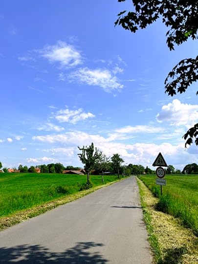 Eine ländliche Straße iin Nordostwestfalen, Apfelbäume am Straßenrand, blauer Himmel, weiße Wolken
