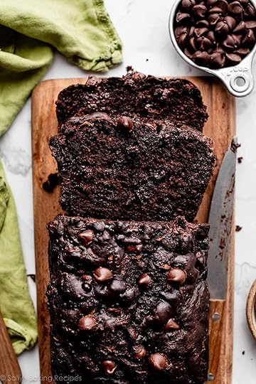 loaf of chocolate zucchini bread with chocolate chips cut with 2 slices on wooden cutting board.