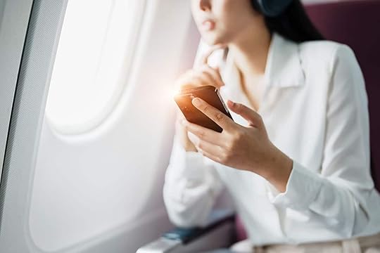 Woman on airplane looking out the window, holding her phone to do an EFT Tapping meditation for fear of flying