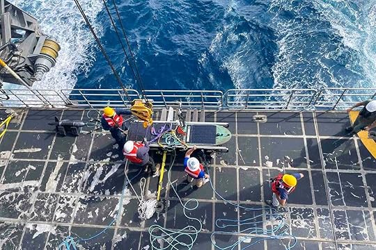 A look above sailors and other people working with equipment on the deck of a ship.