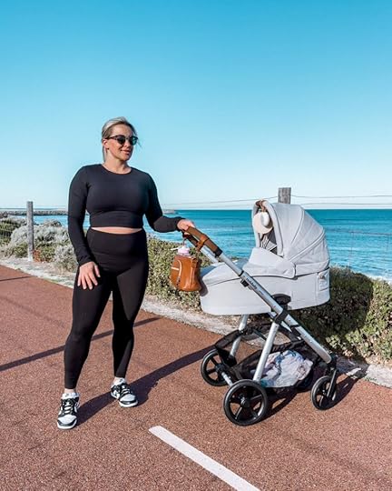 Blonde woman in black activewear with pram on footpath near beach.