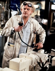 Doc Brown from Back to the Future holding an oversized plug, wearing goggles and a dirty lab coat. 