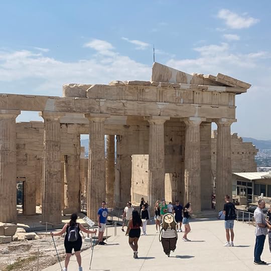 A photo of some of the ruins around the Acropolis. Tourists are all around and it's a sunny day. An illustration of myself is among the crowd, walking towards the camera.