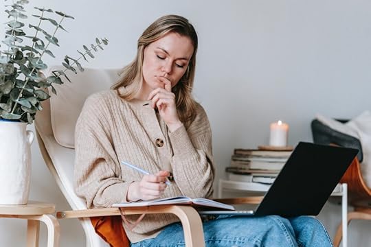 A thoughtful woman writing notes while working with her laptop.
