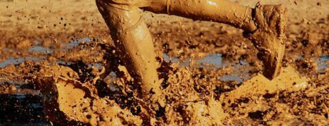 Photo of a person's mud-splattered legs running through a deep muddy puddle for the concept of 