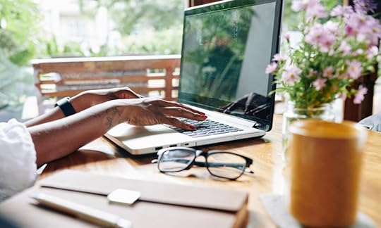 woman's hands typing on a laptop keyboard with reading glasses and a vase of flowers in foreground; how long does it take to write a memoir