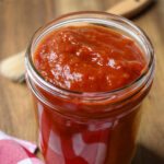 jar of BBQ sauce on table with red checked cloth and a basting brush.