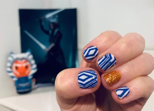 In the background is an issue of Star Wars Insider with Ahsoka Tano on the cover, wielding her two lightsabers, and standing in front of the magazine is a Hallmark Itty Bitty Ahsoka plush figure. In the foreground is a hand with Ahsoka-inspired nails. Four of the nails are the blue/white pattern of Ahsoka's lekku, and one is a copper-colored accent nail. (Nerd manicure by Espionage Cosmetics.) 