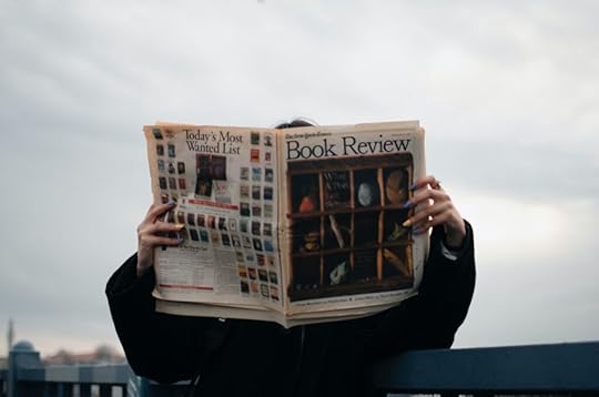 A person holding a newspaper with a book review on the cover.
