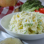 bowl of dill potato salad on a table with other picnic items.