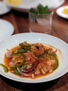 White plate with seafood ceviche and a cocktail in the background