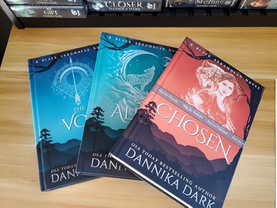 Three books displayed on a desk. Backgrounds of tree and mountain silhouettes and rural vibes with vibrant colors and imagery