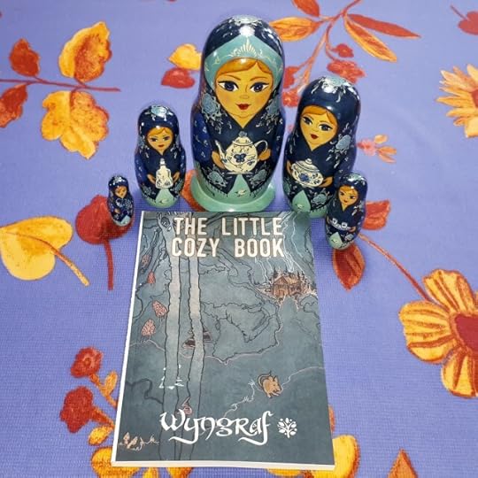 Three friendly Matryoshka dolls cluster around The Little Cozy Book