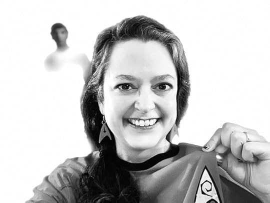 A black and white photo of me, Amy H. Sturgis, in a Star Trek: The Original Series tribute shirt and earrings, with a ghostly image of a Leonard Nimoy-as-Mr. Spock standee peering over my shoulder. 