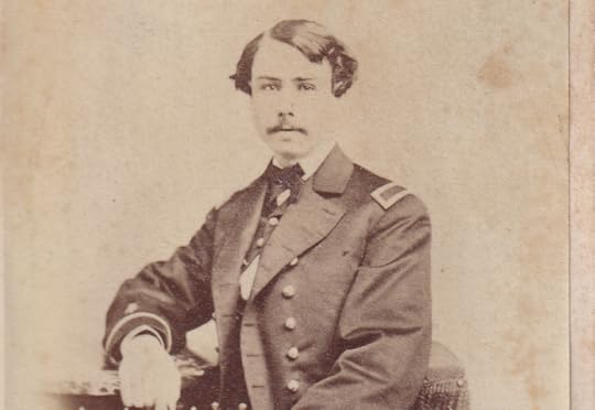 Sepia toned half portrait of John Phelan. A young man, he is seated, wearing a military uniform and is half turned to face the camera. He has a mustache and has a serious expression.