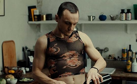 Franz Rogowski wears a mesh crop top with red dragons as he pours wine in