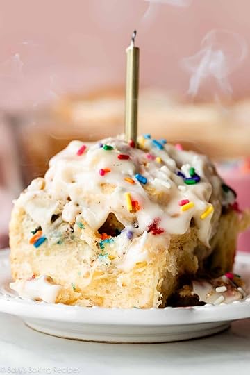 sprinkle funfetti cinnamon roll with cream cheese icing on top and a gold candle blown out.