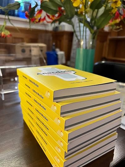 A stack of yellow books with a maxi pad on the cover: Anecdotes by Kathryn Mockler. The books sit beside a bouquet of flowers.