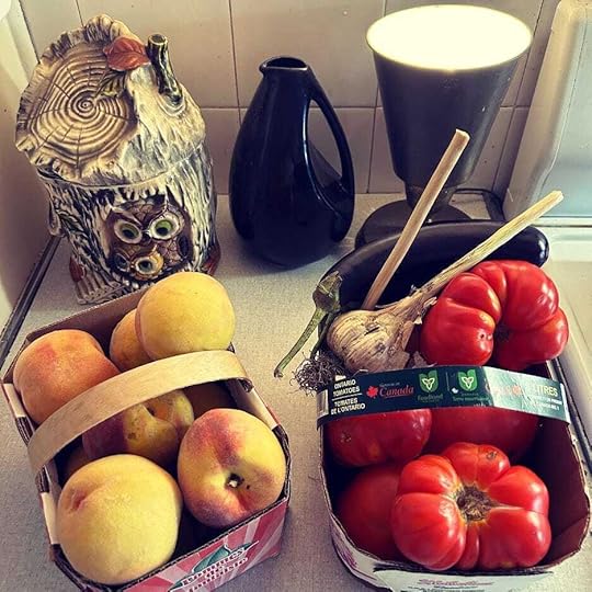 Basket of peaches and basket of tomatoes, eggplant, garlic on a countertop.