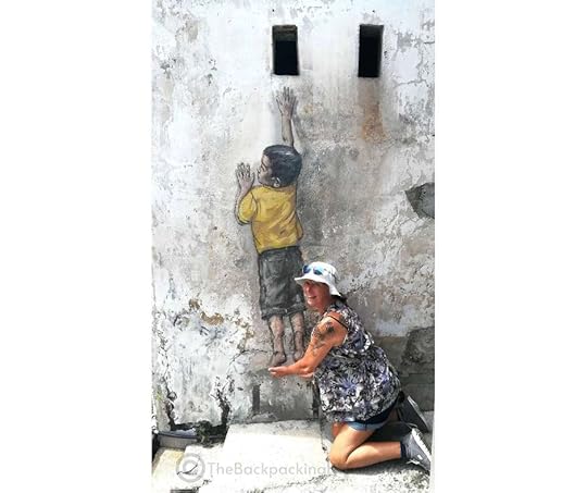 Backpacking Housewife. Reaching Up (by Ernest Zacharevic): This interactive mural can be found on Cannon Street and features a child on a chair reaching for a hole in the wall.