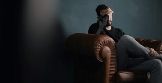 Man who has experienced trauma sitting on a couch holding head in hands
