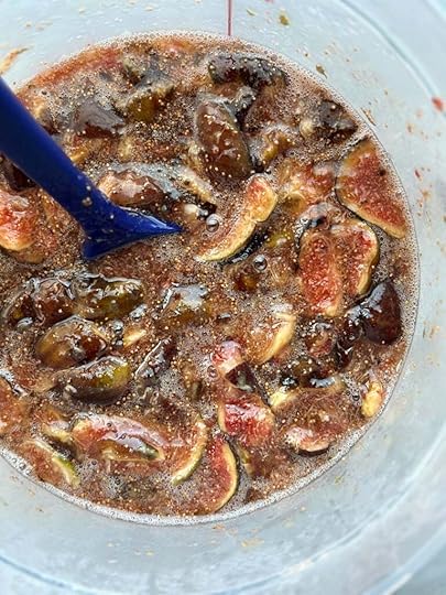 Fresh figs macerated in sugar in a translucent plastic container. There is a blue spatula sticking out of the container.