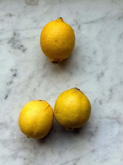 Three bright yellow lemons on a marble countertop.