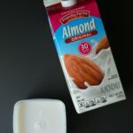 carton of almond milk on black background with small square container of milk ready to freeze.