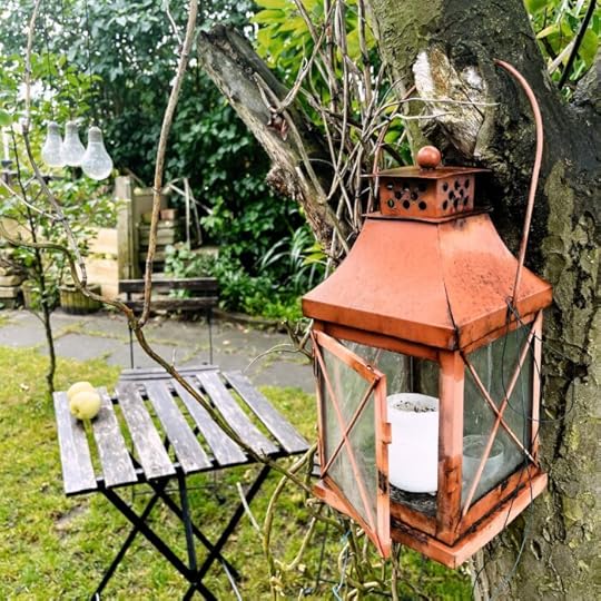Fallobst auf einem Holztisch im Garten, im Vordergrund eine Laterne mit einer Kerze darin an einem Baum