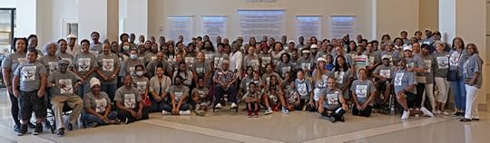 Wide group shot of perhaps 100 people kneeling and standing in a large open space.