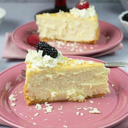 Sliced White Chocolate Cheesecake filling baked with a ladyfinger crust and garnished with whip cream, chocolate curls and berries.