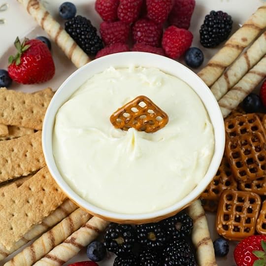 Closeup image of a bowl filled with cheesecake dip with, berries, crackers and pretzels surrounding the bowl.