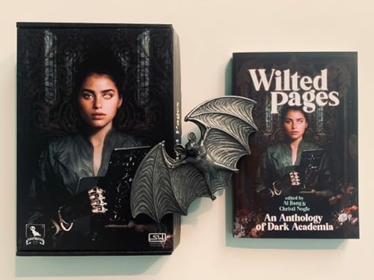 Pictured is the Wilted Pages cover box and the Wilted Pages book, both with the same artwork (depicting in dark, Gothic imagery a woman holding a book or tablet with one human hand and one mechanical or cyborg hand, looking at the viewer with one organic eye and one apparently synthetic eye); a carved bat rests on top of and joins the book cover and book. Photo by AHS.