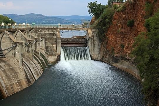 Sluice gate of a dam pouring water into a river, with mountains in the background