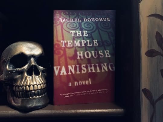 Shown is a skull in a bookcase with a copy of THE TEMPLE HOUSE VANISHING, with cover art depicting wrought-iron gates. Photo by AHS.